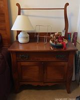 Side view of wooden washstand with items on top (lamp, book holder, and decorative bowl with flowers).
