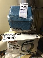 Makita orbital sander in blue packaging with label, stacked on portable halogen lamp box.