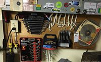 Overall view of various tools mounted on a wall and laid out, showing wrenches, screwdrivers, drill bits, and a wire brush.