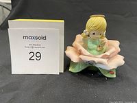 Front view of the porcelain figurine depicting a blonde girl in a green dress sitting inside a pink flower with a rabbit on her lap and a ladybug on a leaf below.