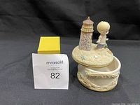 Photo showing the full music box figurine, child with lighthouse on sandy base with seashells