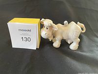 Front view of the white cartoonish cow figurine sitting on black surface with seller's handwritten sign 130 in the background.