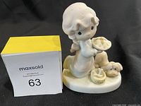 Front and side view of white porcelain figurine depicting child holding decorated plate, with a dog and basket on base.