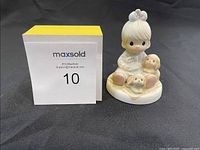 Front view of Precious Moments figurine next to a MaxSold marker showing item number 10.