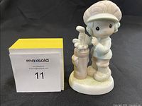 Front view of the Precious Moments figurine featuring the boy golfer standing next to the golf bag with clubs.