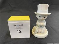 Front view of the figurine showing a child dressed in a suit and white top hat holding hands together on a round base.
