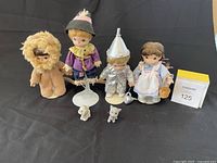 Four Precious Moments Wizard of Oz character figurines and two small dog figurines shown on black background.