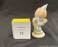 Front side view of the Precious Moments figurine showing the angel holding flowers with white cone hat and wings.