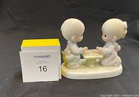 View of porcelain Precious Moments figurine with a boy and girl assembling a puzzle at a small table on an oval base.