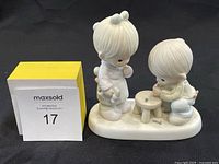 Full view of the Precious Moments figurine showing two children playing with a small stool, one standing and giving thumbs up, the other kneeling.