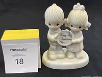 Front view of the Precious Moments Happy Anniversary 1983 figurine showing the boy and girl holding the plaque.