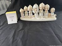 Front view of the figurine showing seven child characters and two dogs on a white base, with a size reference card.