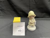 Front view of the Precious Moments figurine with a child holding a lamb and wearing a yellow raincoat and hat.
