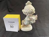 Precious Moments ceramic figurine holding a doll with a yellow box and auction lot card numbered 50
