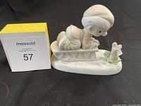 Front side view of Precious Moments 1993 Christmas figurine with child on sled and wrapped gift, placed next to lot number card.