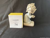 Photo of the figurine showing front and side profile with a MaxSold lot number 74 card next to it for scale and identification.