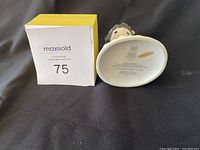 Photo of the bottom of the figurine showing markings and year 1993, resting on black fabric beside an original yellow and white box with lot number sticker.