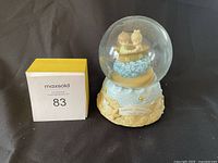 Photo of snow globe music box showing two children figurines in a boat inside the globe and inscription on base.