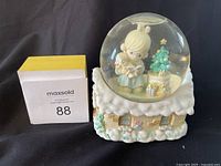 Precious Moments music box figurine with girl holding teddy bear inside snow globe on snowy house base.