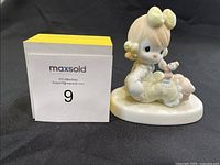 Side view of Precious Moments figurine next to MaxSold number card