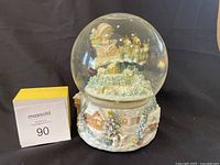 Front view of Precious Moments Oh Holy Night snow globe figurine showing Santa sleigh with reindeer flying above snowy village base.