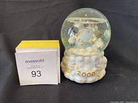 Photo of Precious Moments 2000 snow globe figurine with 'Id Like To Teach The World To Sing' theme and white sculpted base.