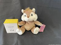 Photo showing a single Precious Moments plush chipmunk sitting upright on a dark surface in front of a grey background with a MaxSold lot number block beside it.