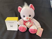 Light purple Precious Moments plush bear seated on a dark fabric background with original tag positioned beside it and a MaxSold lot number block.
