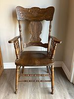 Front view of antique pressback armchair showing hand carved floral and scrollwork design on the high curved backrest and turned spindle construction.