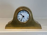 Front view of solid brass mantle clock showing white face with Roman numerals and black clock hands at 10:38.