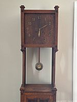 Front view of clock showing square clock face, open mid section, and lower cabinet.