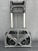 Front view of the collapsed furniture dolly showing metal frame, black two ergonomic handles, and wheels folded inside base.