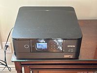 Front angled photo of Epson XP-6100 printer showing the power button, LCD display, keypad, and branding on glossy front panel.