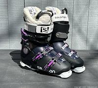 Pair of black ladies Solomon ski boots with purple buckles and white accents on grey wooden floor.