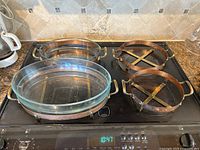 Photo showing three oval baking dishes with removable Pyrex glass inserts in copper and brass handles stands, plus two additional copper stands without glass