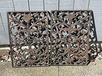 Both identical cast iron door grates side by side against a light gray wall.
