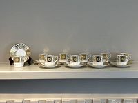Set of 10 espresso cups and saucers arranged in line showing Green Derby Panel pattern with green floral panels and gold accents on bone china.