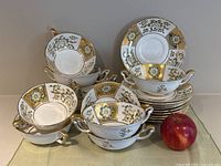 Five double-handled soup bowls paired with saucers and apple for scale