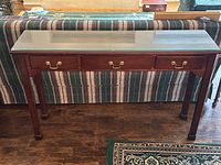 Front view of the console table showing three drawers with brass pulls, beveled glass top and wooden frame.