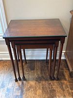 Set of three wooden nesting tables stacked together showing size progression with largest table having glass top.