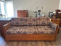 Front view of vintage pine framed sofa with floral patterned cushions and pullout mechanism.