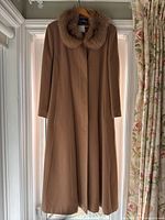 Full view of the brown wool women's coat hung on a hanger, displayed in a well-lit room with floral curtains in the background.