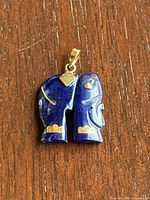 Front side view of the lapis lazuli and 14K gold elephant pendant showing the deep blue stone with gold accents on a wooden surface.