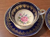 Close-up of an Aynsley tea cup with a cobalt blue border, intricate gold pattern, and a floral design inside the cup.