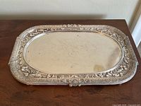 Top view of antique silver plated tray showing the mirrored center and decorative floral border with visible scratches and wear.