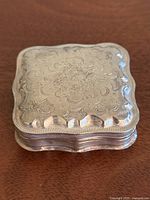 Top view showing detailed floral and scroll engraved pattern on the lid of the silver snuff box.