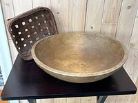 Front angled view showing wooden dough bowl and woven basket behind it on black surface with wood-paneled background.