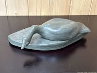 Hand-carved soapstone goose sculpture resting on a dark surface showing the grey natural stone finish and smooth texture.