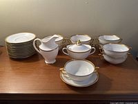 Overall view of the lot showing the 10 Limoges soup bowls with saucers, Royal Doulton cream and sugar set, and other items.