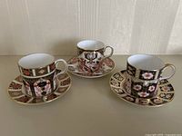 Front view of set of three Royal Crown Derby Imari demitasse cups with matching saucers arranged in a row.